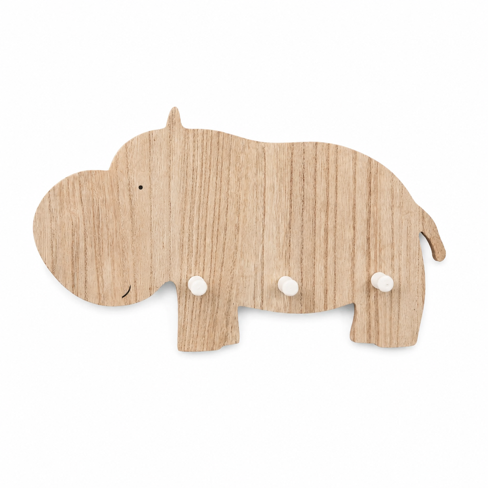 A light natural wood hippo-shaped wall hook rack mounted on a beige wall, with three hanging accessories: a cream drawstring bag, a sage green textured cloth, and a small wooden camera bag.