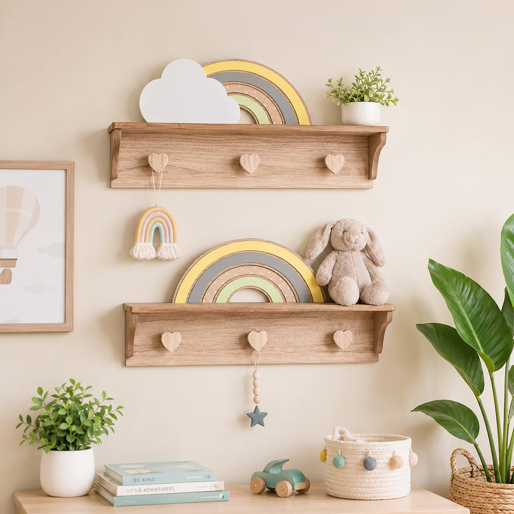 Two light natural wood wall shelves styled in a nursery setting, decorated with a wooden rainbow, a white cloud cutout, a small potted plant, a plush bunny toy, and heart-shaped peg hooks.