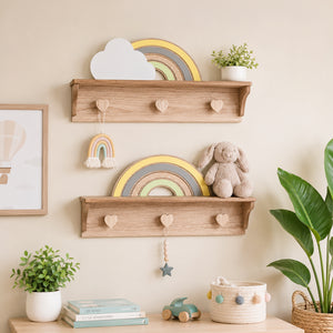 Two light natural wood wall shelves styled in a nursery setting, decorated with a wooden rainbow, a white cloud cutout, a small potted plant, a plush bunny toy, and heart-shaped peg hooks.