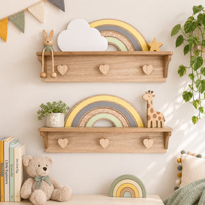 Two light natural wood wall shelves with heart-shaped pegs, styled in a nursery setting with toys, a plant, books, and a teddy bear against a warm off-white wall.