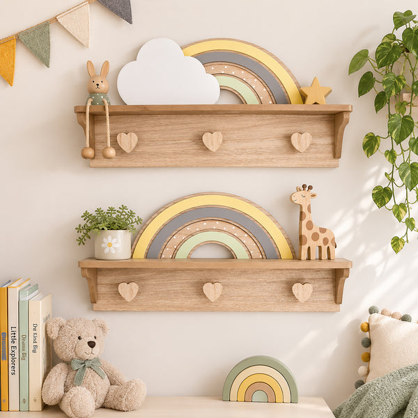 Two light natural wood wall shelves with heart-shaped pegs, styled in a nursery setting with toys, a plant, books, and a teddy bear against a warm off-white wall.