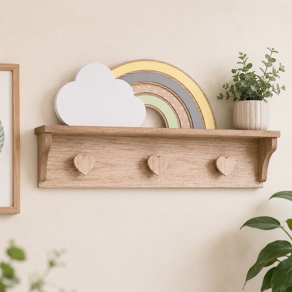 A light natural wood floating shelf mounted on a beige wall, styled with a white cloud decoration, a pastel rainbow, and a small potted green plant.