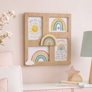 A square natural wood picture frame with four inset panels decorated with colorful children's artwork, including suns, rainbows, clouds, and inspirational quotes, displayed on a pale pink wall above a styled shelf.