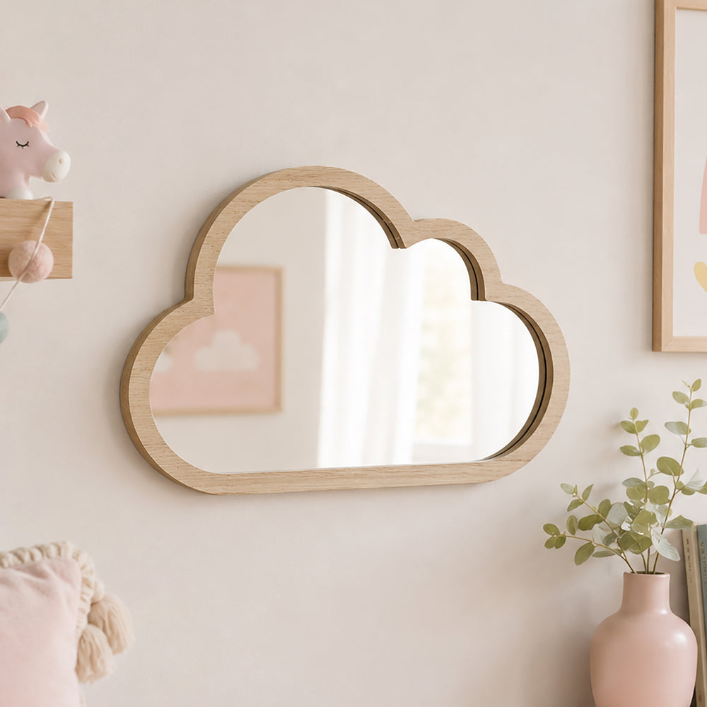 A cloud-shaped wooden wall mirror with a light natural oak frame, mounted on a warm beige wall in a styled nursery or children's room setting.