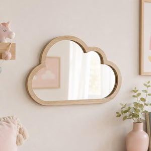 A cloud-shaped wooden wall mirror with a light natural oak frame, mounted on a warm beige wall in a styled nursery or children's room setting.