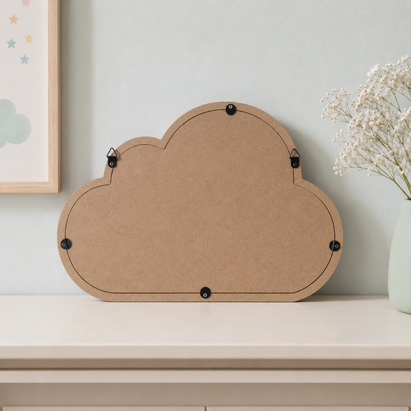 A cloud-shaped cork board with black metal clips on the back, displayed on a light beige shelf against a pale blue-gray wall, with a vase of baby's breath and a framed print partially visible.