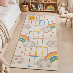 A children's play rug featuring a hopscotch layout with numbers, rainbows, clouds, and hearts on a cream background, styled in a child's bedroom.