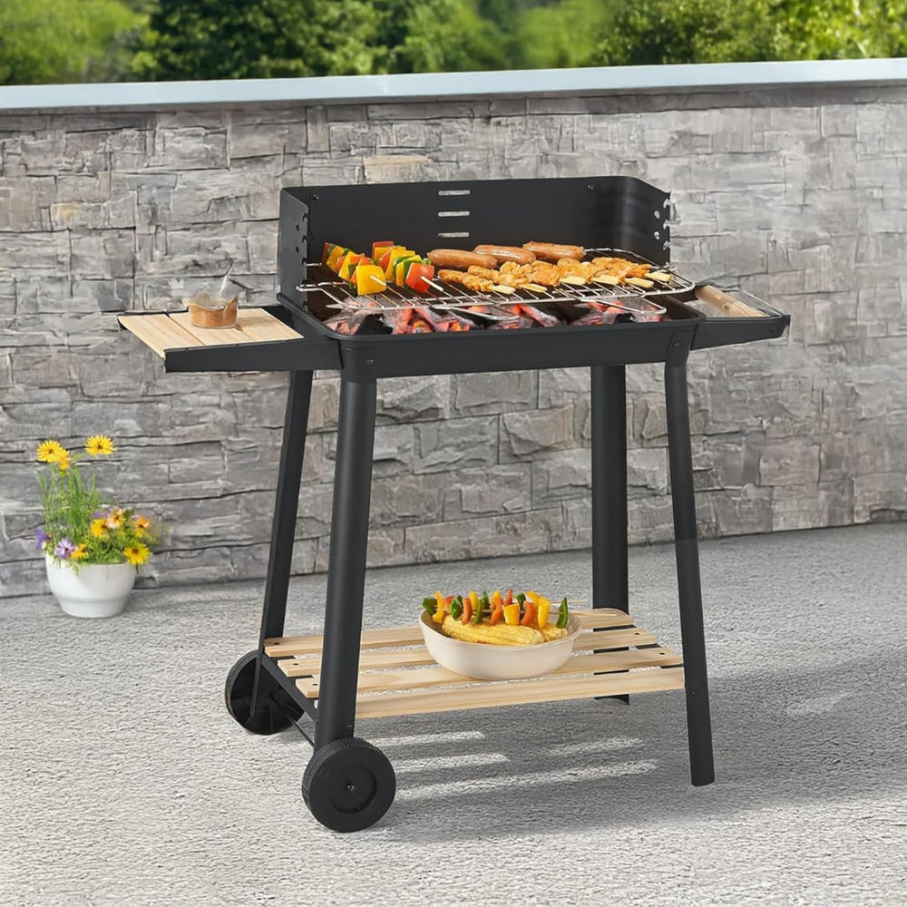 A black and wood outdoor charcoal grill with wheels, shown cooking food on a patio in front of a gray stone wall.