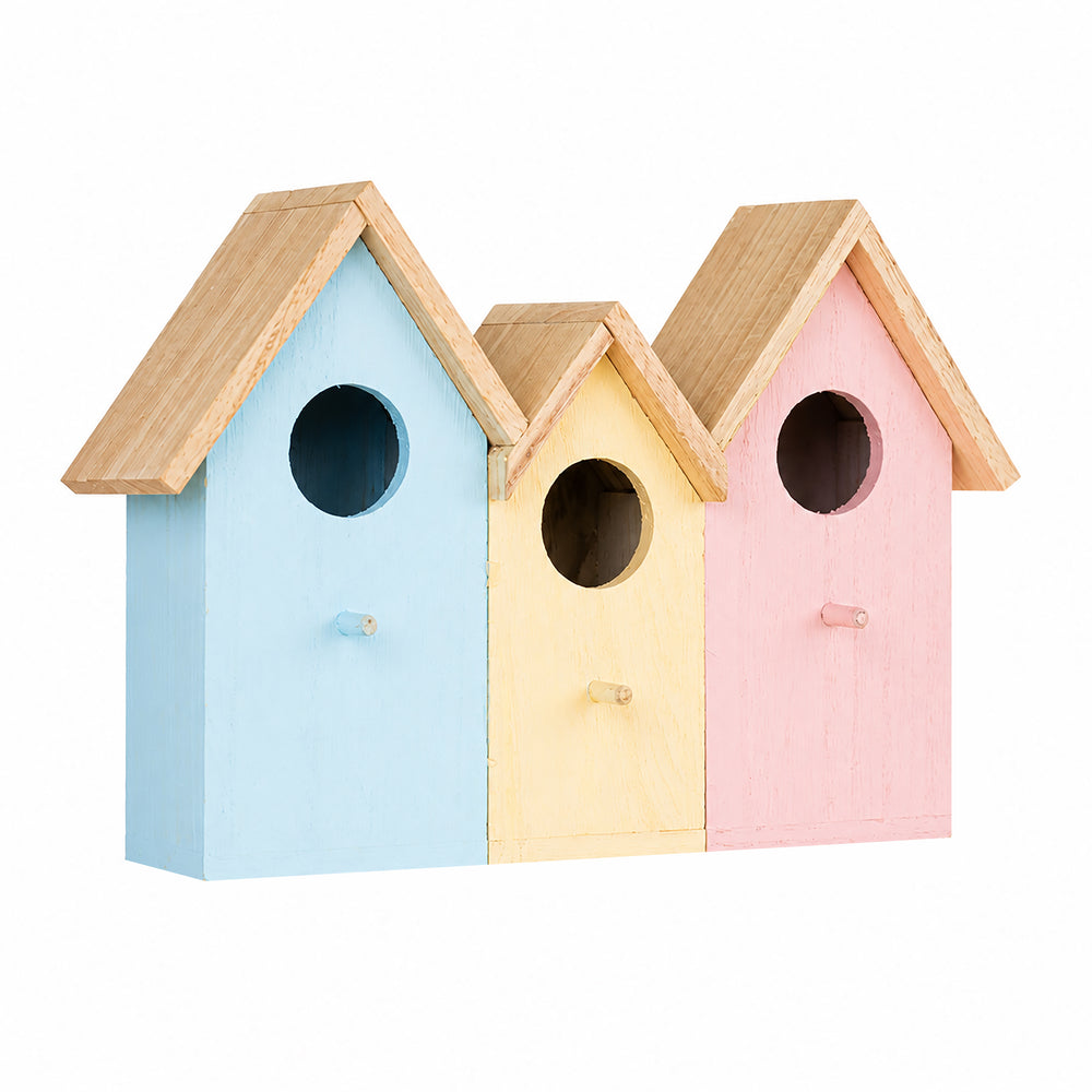 Three small house-shaped birdhouses in pastel blue, cream, and pink are mounted on a tree trunk outdoors, with a small bluebird perched on the right birdhouse.