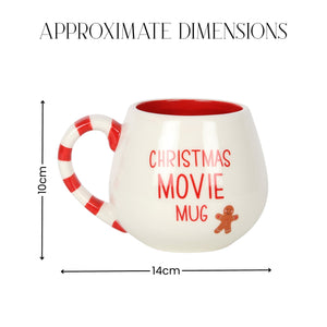 A white ceramic mug with a red interior and red-and-white striped handle, shown with dimension lines and text indicating approximate dimensions of 14 cm wide by 10 cm tall. The mug has the words 'CHRISTMAS MOVIE MUG' in red and a small gingerbread figure graphic.