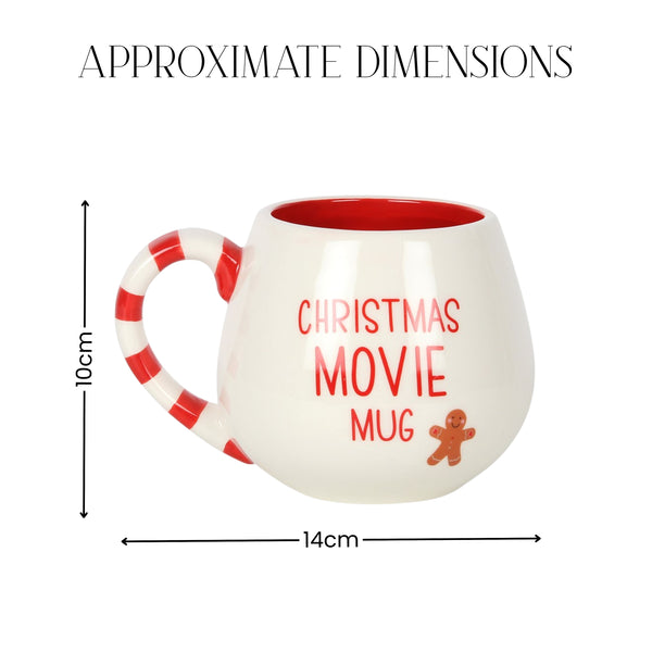 A white ceramic mug with a red interior and red-and-white striped handle, shown with dimension lines and text indicating approximate dimensions of 14 cm wide by 10 cm tall. The mug has the words 'CHRISTMAS MOVIE MUG' in red and a small gingerbread figure graphic.