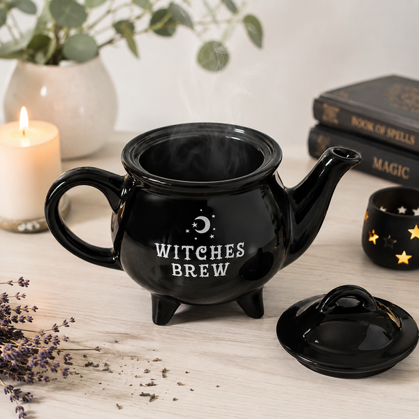 Glossy black Witches Brew ceramic teapot with matching lid, styled on a wooden table with candle, books and dried lavender.