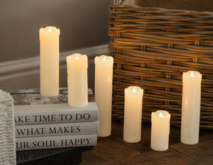 Set of lit candles on a surface with a wicker basket and books in the background.