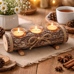 A rustic log-shaped candle holder with three lit tealight candles, wrapped in twine and tied with a bow, set on a burlap-covered wooden table with warm holiday decor in the background.