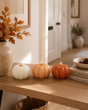 Three decorative miniature pumpkins in white, peach, and orange arranged on a wooden console table in a warm, styled interior setting.