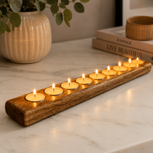 A rustic wooden candle holder with nine slots, each holding a lit tealight candle, placed on a white marble surface in a styled interior setting with books and a vase in the background.