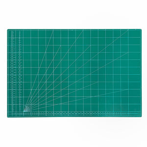 A square green cutting mat with a white grid, measurement markings, and diagonal guide lines radiating from the bottom-left corner, shown on a plain white background.