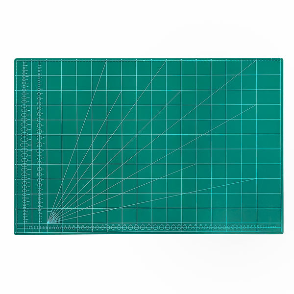 A square green cutting mat with a white grid, measurement markings, and diagonal guide lines radiating from the bottom-left corner, shown on a plain white background.