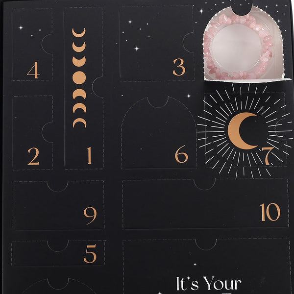 Black advent calendar with gold numbers and moon phases, featuring a pink treat on one of the doors.