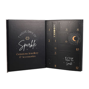 Open black advent calendar with gold text and designs, featuring 'Twelve Days of Sparkle' jewellery and accessories theme.