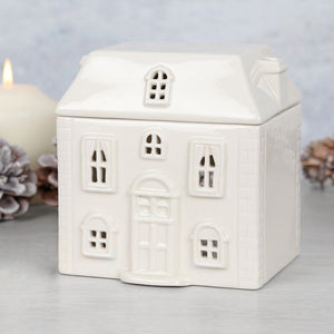 White ceramic house-shaped lantern with a candle inside on a light gray background