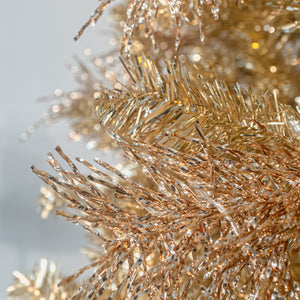 Close-up of shiny metallic gold tinsel or decorative garland strands against a soft light gray background.