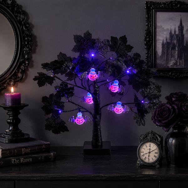 A gothic-style tabletop display featuring a black metal tree with glowing purple and pink spider-shaped string lights, styled in a dark room with a candle, books, framed artwork, and a small clock.