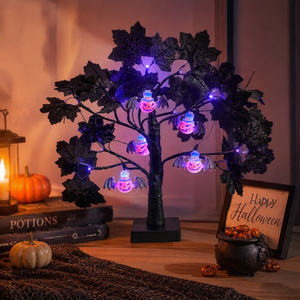 A Halloween decorative tree with black leaves and glowing purple fairy lights, styled on a tabletop with pumpkins, a lantern, books, and a small 'Happy Halloween' sign.