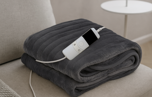Grey heated blanket with digital dial to control, placed on beige sofa.
