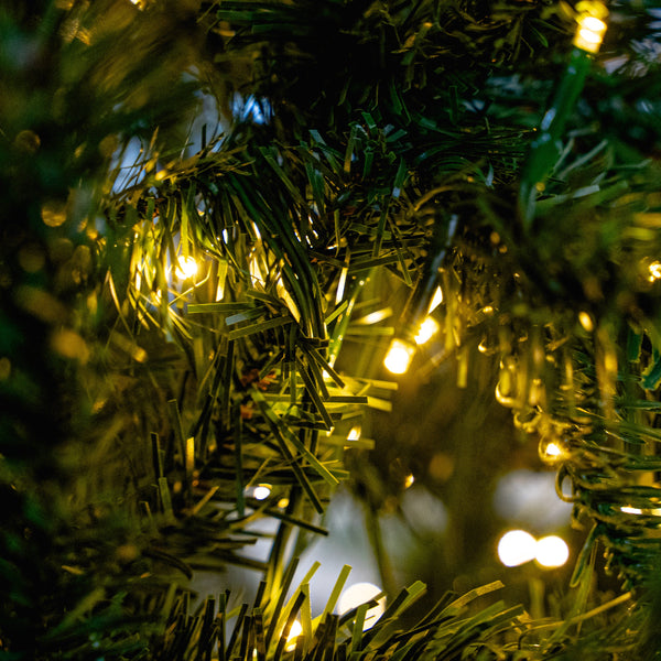 Close-up of green artificial pine branches with warm white string lights glowing through the needles.