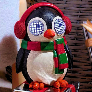A penguin figurine wearing red earmuffs and a green and red striped scarf, with its eyes glowing blue and white, standing on a reflective surface.