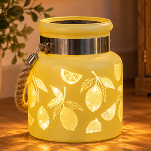 A glowing yellow lantern with a rope handle and lemon cutout patterns, shown on a wooden surface with warm ambient light.