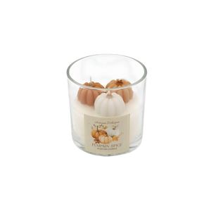 A 'Pumpkin Spice' scented candle in a clear glass jar, decorated with three small decorative pumpkins (two orange and one white) on top of white wax. The candle features a cream-colored label with illustrations of pumpkins.