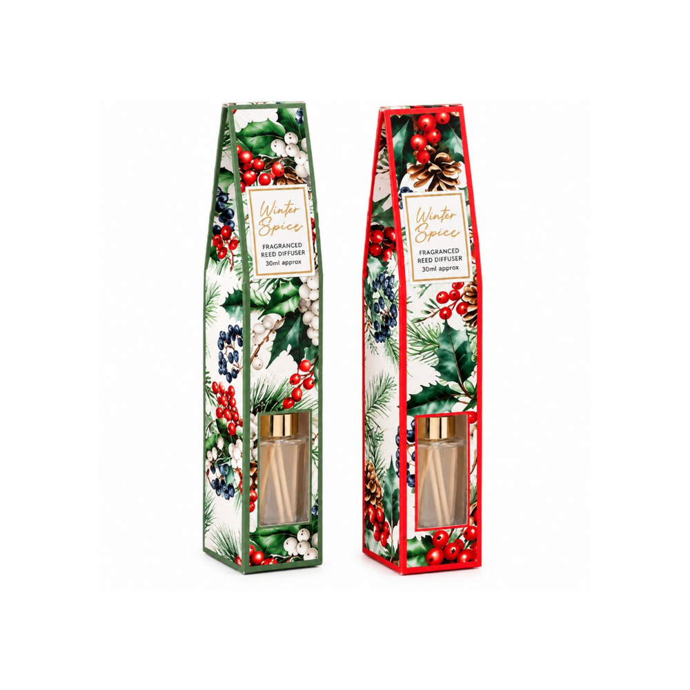 A packaged Winter Berries fragranced Reed Diffuser sits on a wooden table in a cozy holiday setting, with a blurred Christmas tree and warm lights in the background and a wrapped gift box beside it.