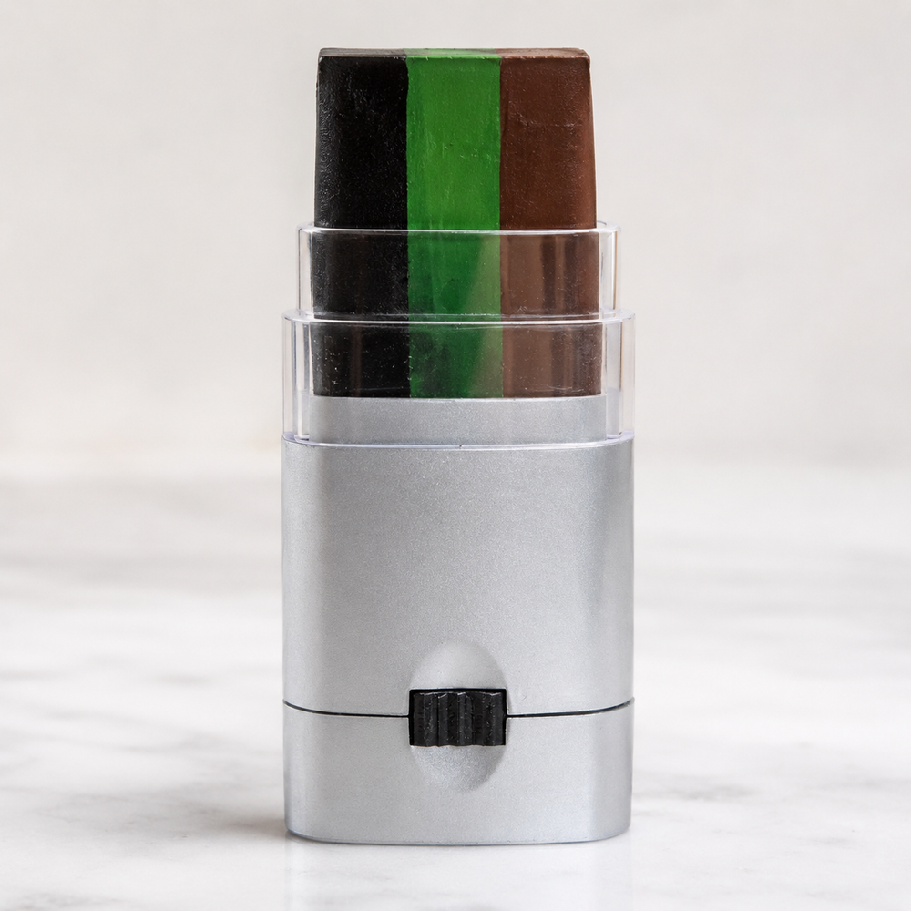 Color swatch stick with green and brown shades on a textured surface, next to a camouflage-patterned fabric and a container of paint.
