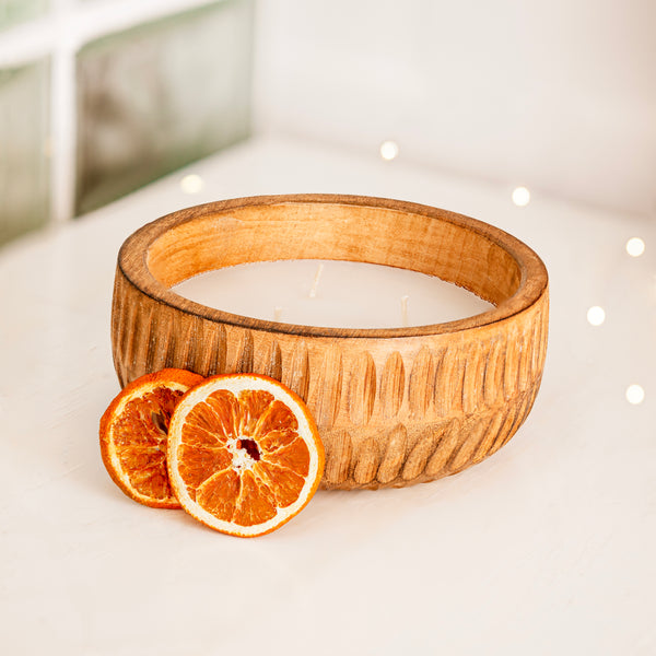 Wooden bowl with a candle and dried orange slices on a light surface.