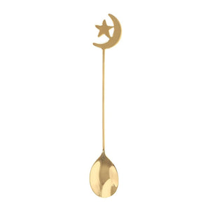 A gold-colored metal spoon with a crescent moon and star cutout at the top, shown vertically against a plain white background.