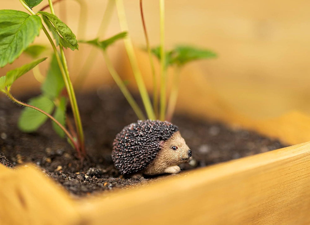 A small artificial trellis designed to look like a hedgehog, with a blurred object in the background that resembles a garden ornament.