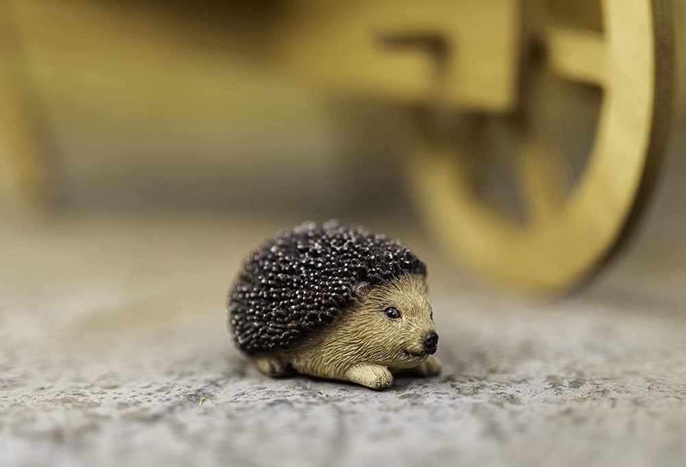 A small artificial trellis designed to look like a hedgehog, with a blurred object in the background that resembles a garden ornament.