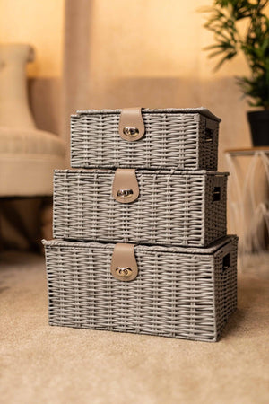 Set of three gray wicker storage baskets with handles on a beige surface.