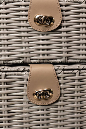 Close-up of a wicker basket with beige leather handles featuring gold hardware.