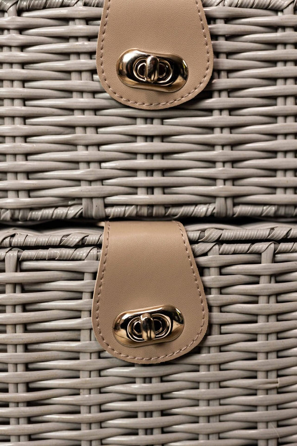 Close-up of a wicker basket with beige leather handles featuring gold hardware.