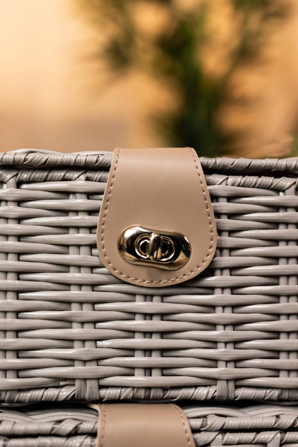 Wicker basket with a beige leather handle and clasp against a blurred natural background