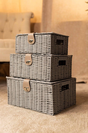 Three gray woven storage baskets with leather straps stacked on a carpeted floor.