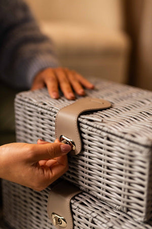 Person opening a wicker suitcase with a hand on a blurred background