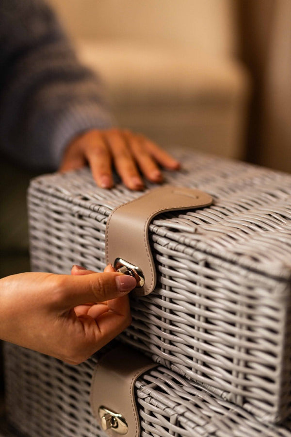 Person opening a wicker suitcase with a hand on a blurred background