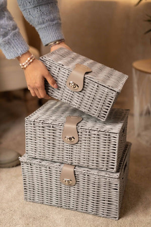 Stack of gray wicker storage boxes with handles on a carpeted floor.
