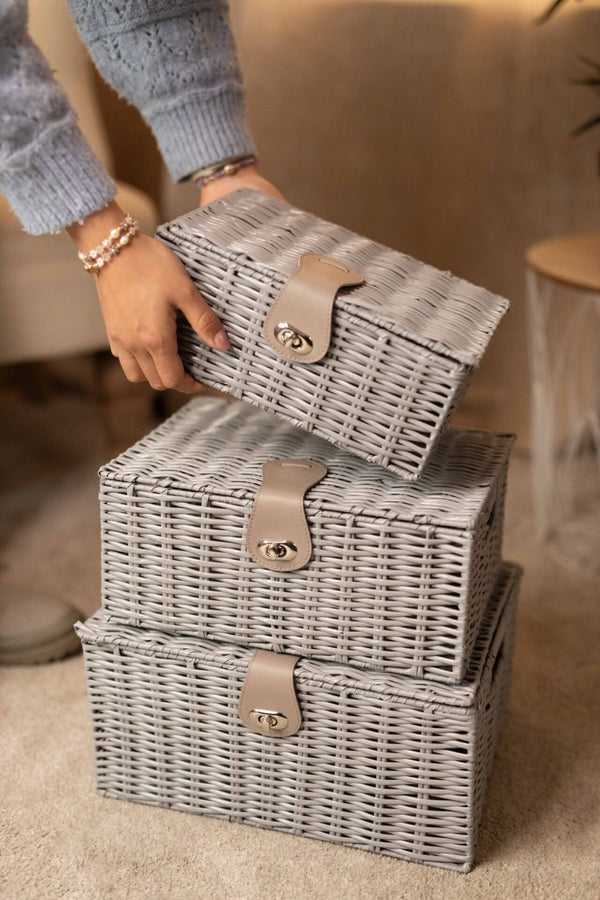 Stack of gray wicker storage boxes with handles on a carpeted floor.