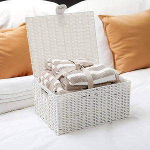 White wicker basket filled with folded towels on a bed with orange pillows.