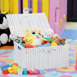 White wicker toy basket filled with colorful toys on a play mat with a colorful playpen in the background.